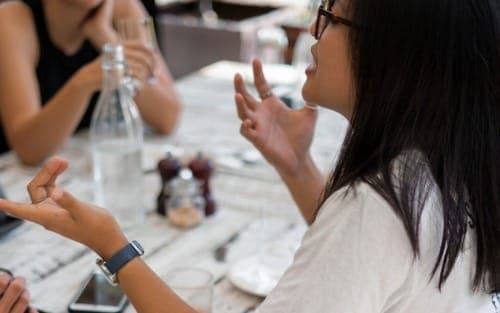 how-to-stop-interrupting-people-woman-at-table-gesturing-speaking